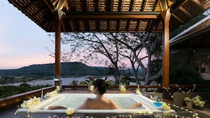 Iemand ontspant in een jacuzzi met uitzicht op een rivier en bergen.