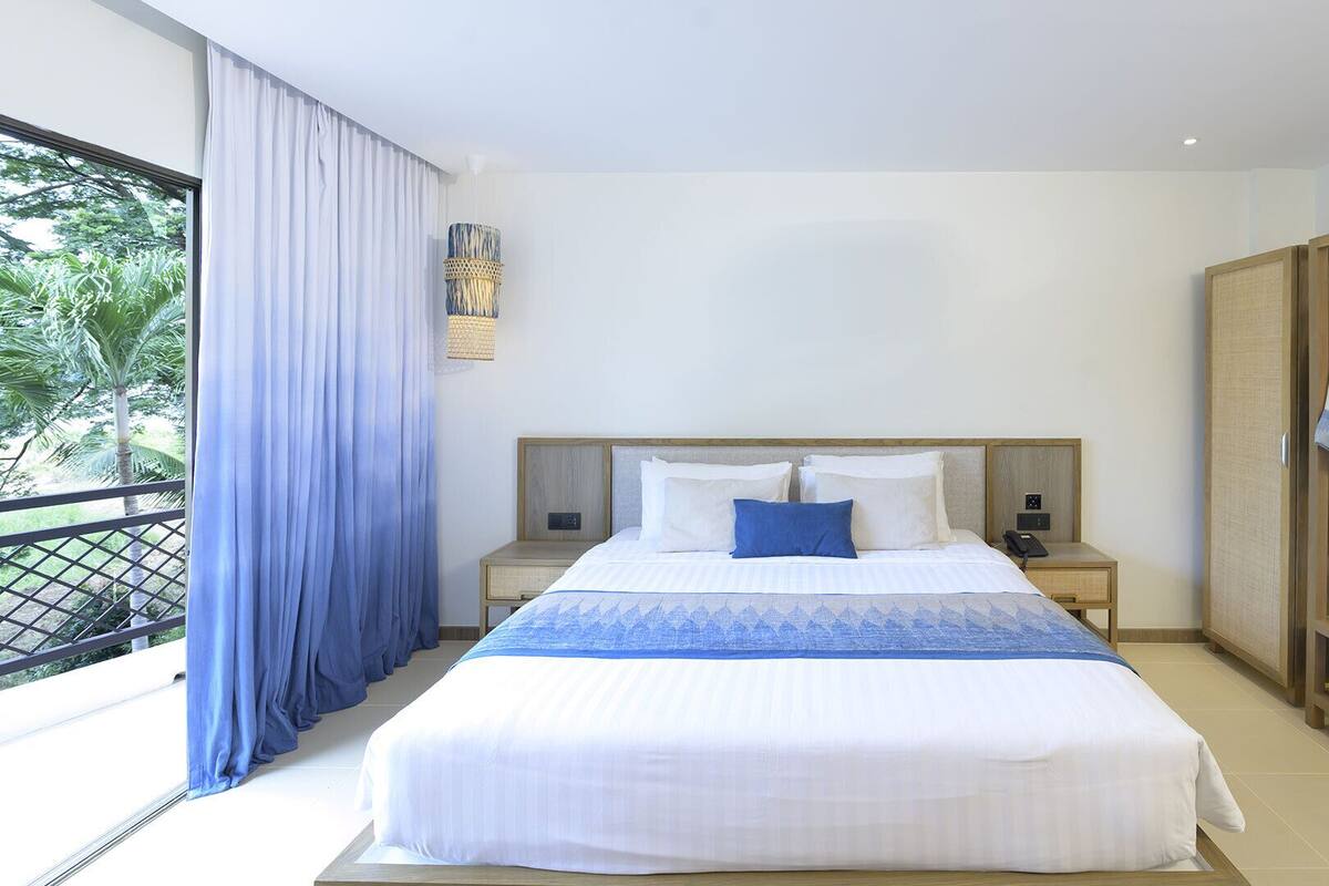 Une chambre d’hôtel avec un grand lit, une table de chevet avec une lampe, une armoire et une vue sur la verdure.