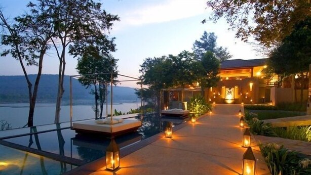 Een luxe resort met een overloopzwembad, terras en een goed verlicht pad naar het hoofdgebouw.