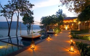Un complexe hôtelier de luxe doté d’une piscine à débordement, d’un espace extérieur aménagé et d’un chemin bien éclairé menant au bâtiment principal.
