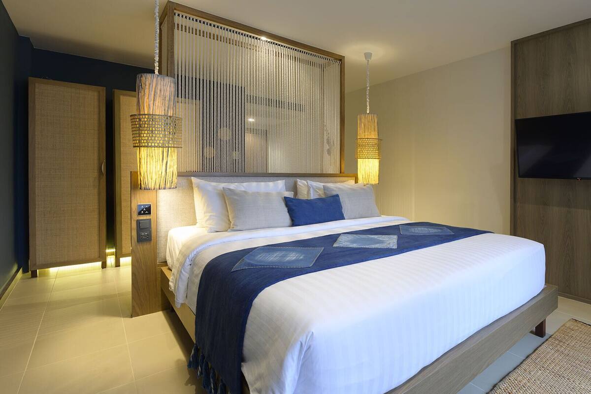 Une chambre d’hôtel moderne dotée d’un grand lit, d’un téléviseur fixé au mur et d’un luminaire décoratif suspendu.