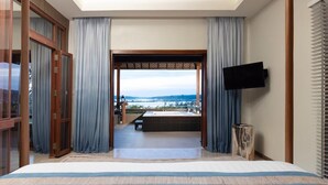 Een slaapkamer met een groot bed, een aan de muur bevestigde televisie, en uitzicht op een balkon met een tafel en stoelen.