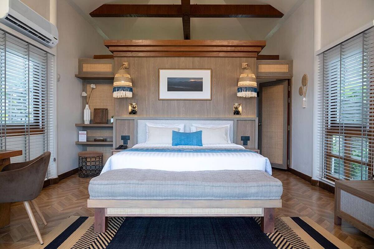 Une chambre à coucher moderne, dotée d’un grand lit, d’une tête de lit en bois et offrant une vue sur l’extérieur grâce à de grandes fenêtres.