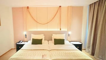 Una cama doble con colcha color beige y dos almohadas, una mesita de noche con teléfono, y un aplique de pared.