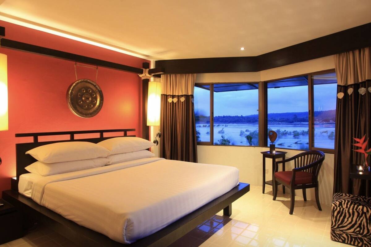 Une chambre d’hôtel avec un grand lit, un bureau avec une chaise et une vue sur un paysage enneigé par de grandes fenêtres.