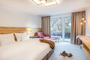 A hotel room with a large bed, a wooden headboard, a plaid armchair, a small table, and a view of a snowy landscape through the window.