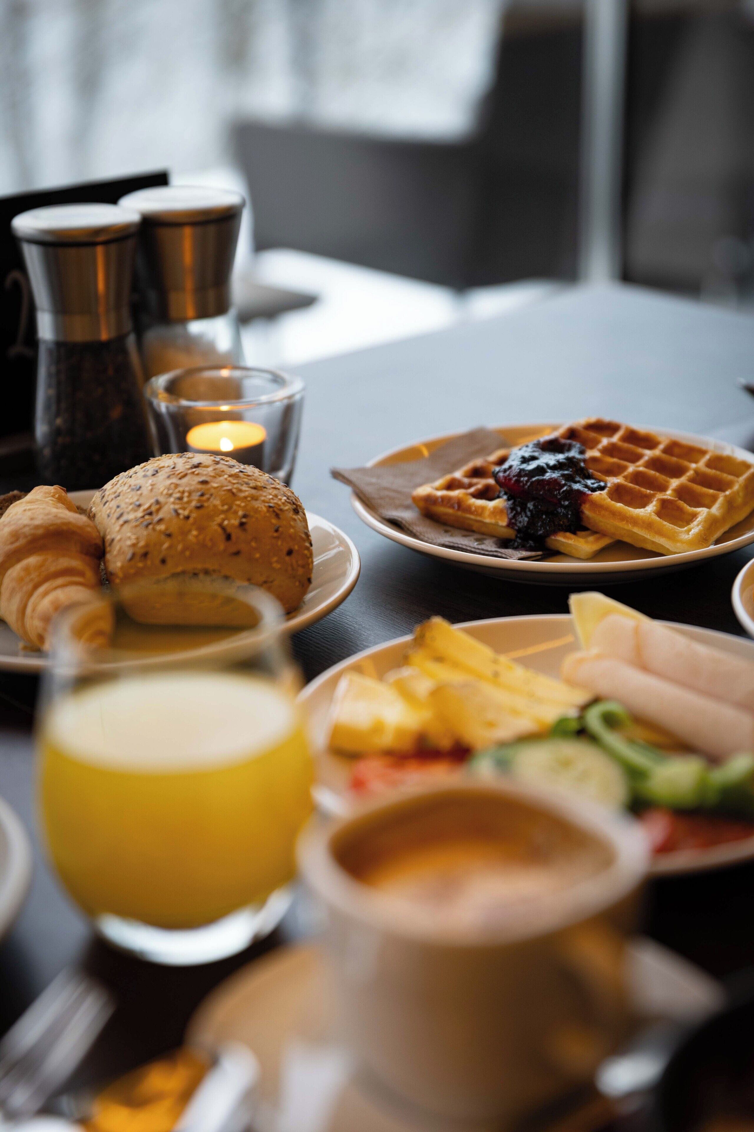 A breakfast table with croissants, waffles, fruit, and a glass of juice.