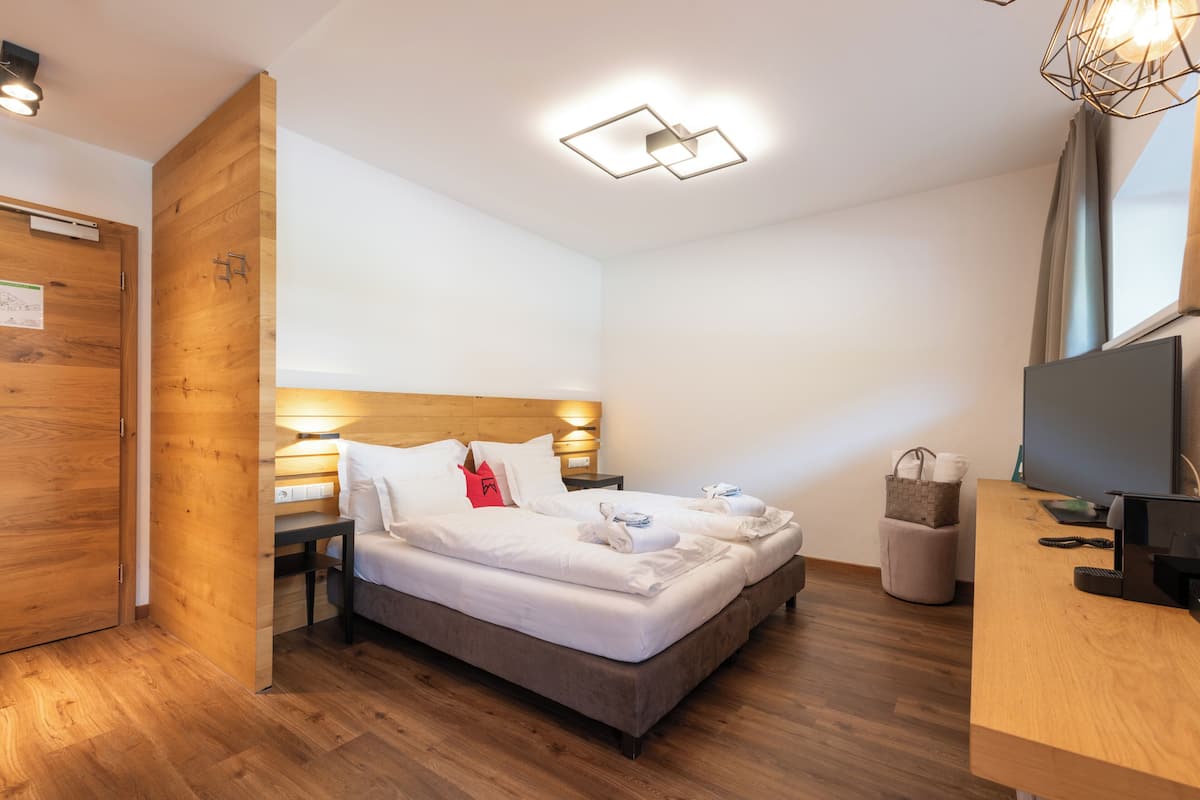 A modern hotel room with a wooden floor, a bed with white linens, a desk with a computer, and a TV.
