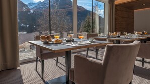 A dining area with tables set for breakfast, large windows offering mountain views, and a modern interior design. - Heart Hotel Grischuna  (Sankt Anton am Arlberg)