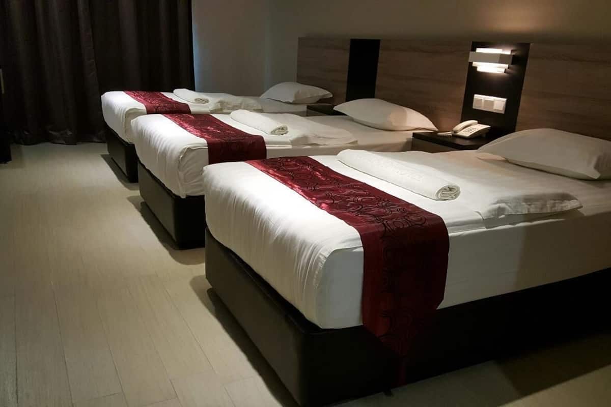 Une chambre d’hôtel avec trois lits, chacun étant équipé de draps blancs et d’une couverture rouge. Une table de chevet avec un téléphone et une lampe se trouve sur le côté droit.