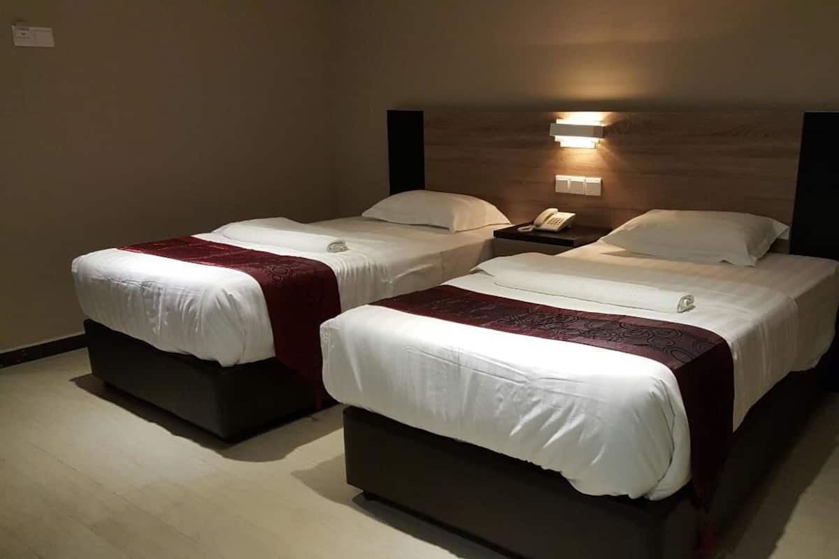 Une chambre d’hôtel avec deux lits, chacun doté d’une tête de lit en bois, de draps blancs et d’un élément décoratif rouge. Il y a une table de chevet avec un téléphone et une lampe.