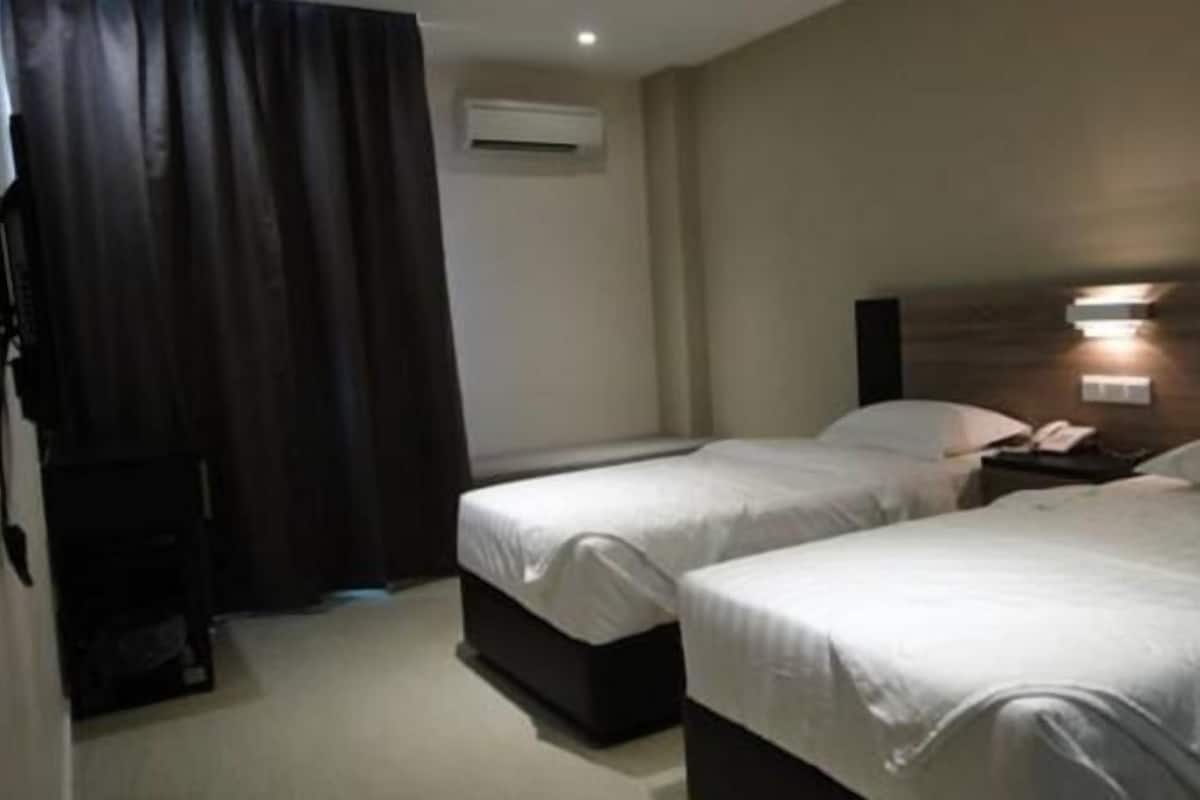 Une chambre d’hôtel avec deux lits, un rideau foncé, un appareil de climatisation et une table de chevet avec une lampe.