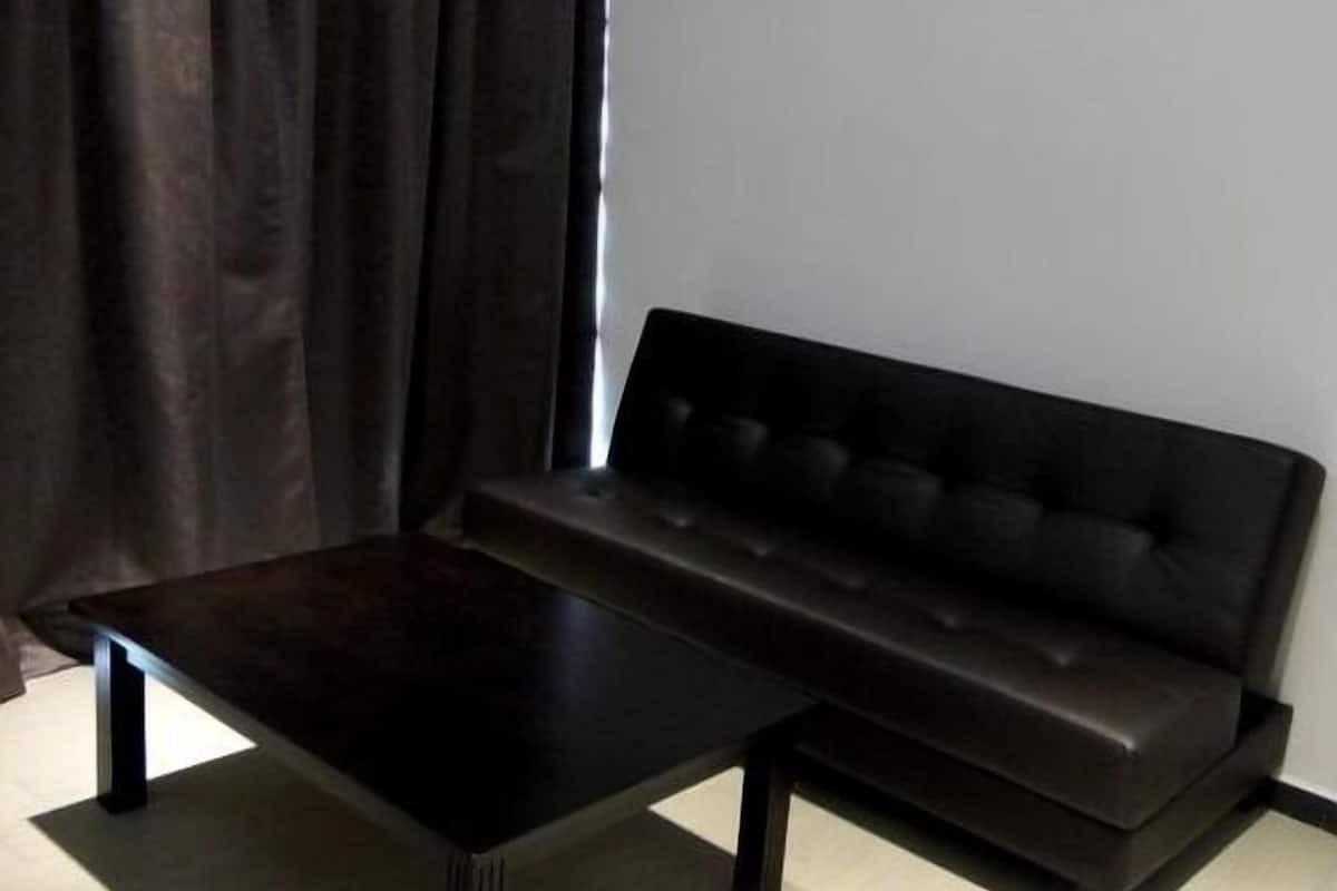 Un canapé marron foncé et une table basse assortie, également marron foncé, se trouvent dans une pièce dont le mur est blanc et qui est agrémentée d’un rideau foncé.