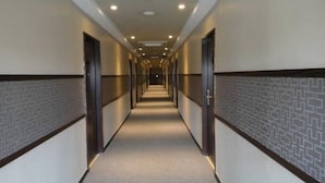 Corredor longo e estreito de um hotel, com portas em ambos os lados e piso coberto de carpete.