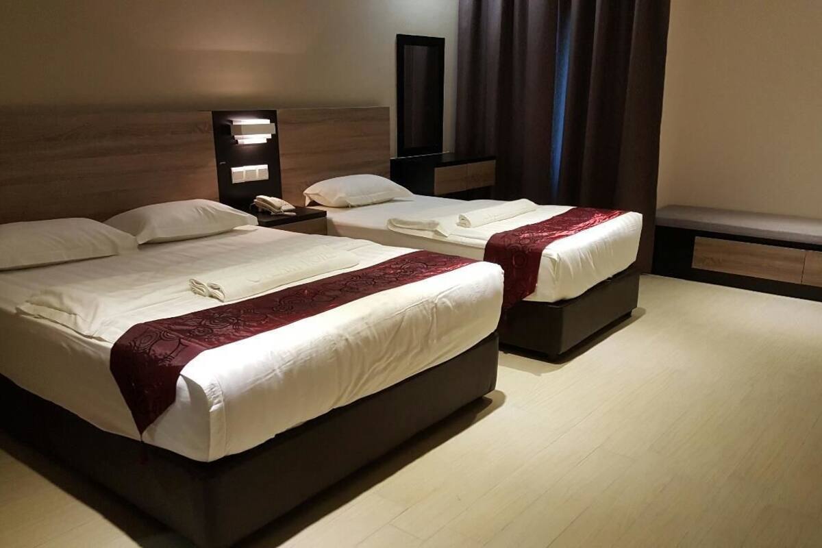 Une chambre d’hôtel avec deux lits, chacun agrémenté de draps blancs et d’un élément décoratif rouge. Une table de chevet, sur laquelle se trouvent une lampe et un téléphone, est placée à côté de l’un des lits.