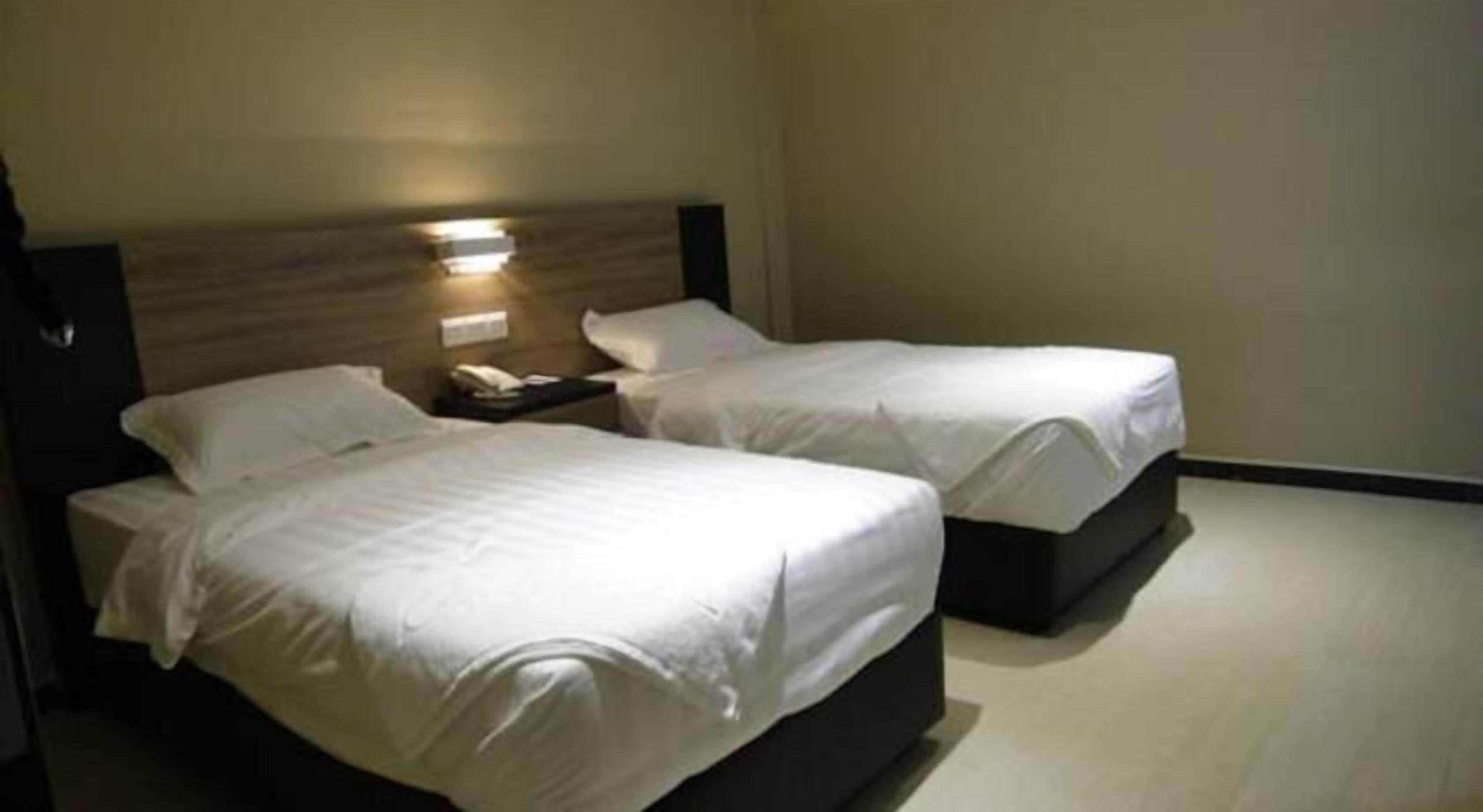 Habitación de hotel con dos camas, una mesita de noche y una lámpara en la pared.