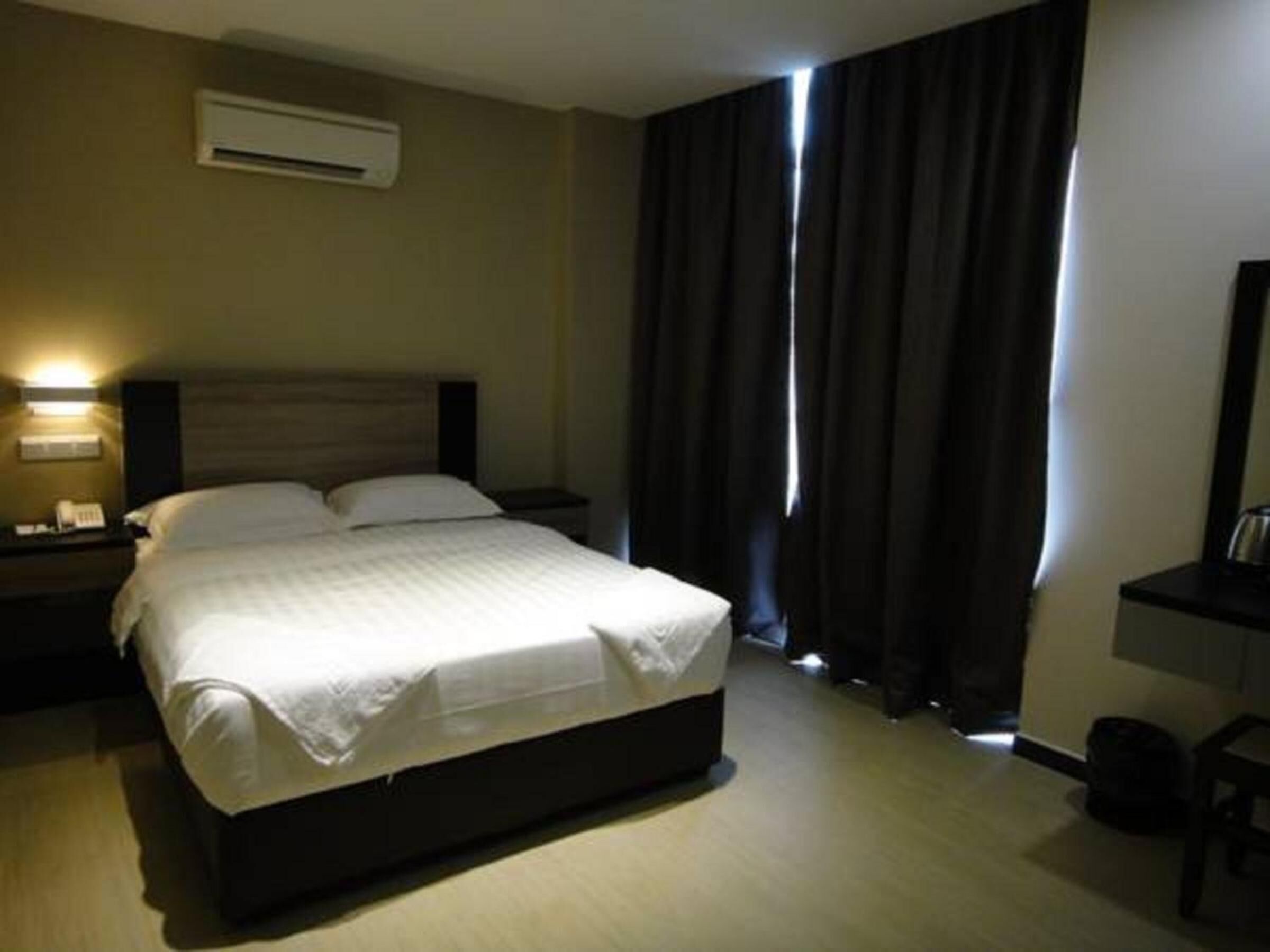 A hotel room with a bed, a nightstand, a desk, and a window with curtains.