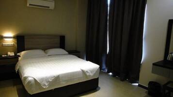 Una habitación de hotel con cama, mesita de noche, escritorio y ventana con cortinas.