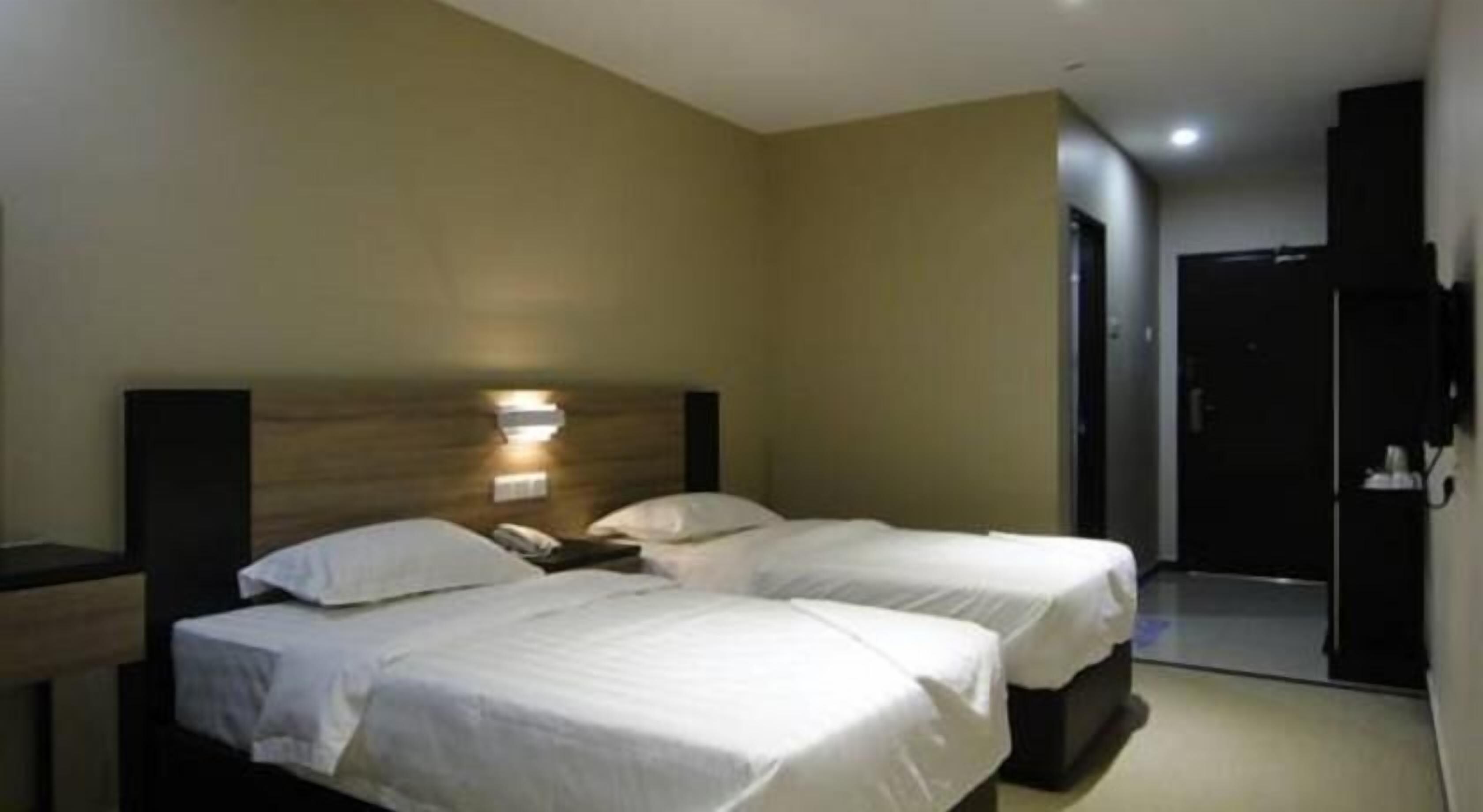 A hotel room with two beds, a bedside table, a wall-mounted light, and a door leading to another room.