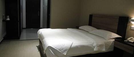 A hotel room with a large bed, a bedside table with a lamp, and a door leading to another room.