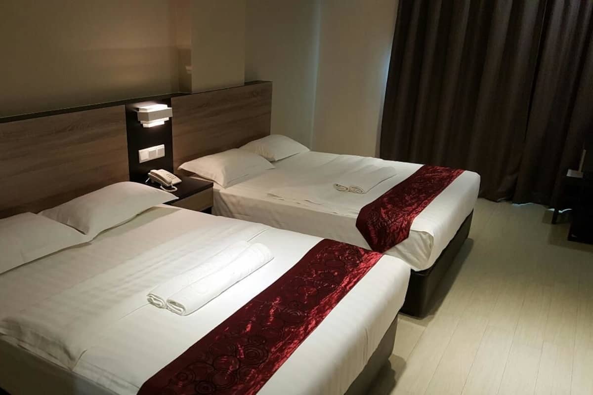Deux lits jumeaux avec du linge de lit blanc et des coussins décoratifs rouges, une table de chevet avec un téléphone et un luminaire fixé au mur.