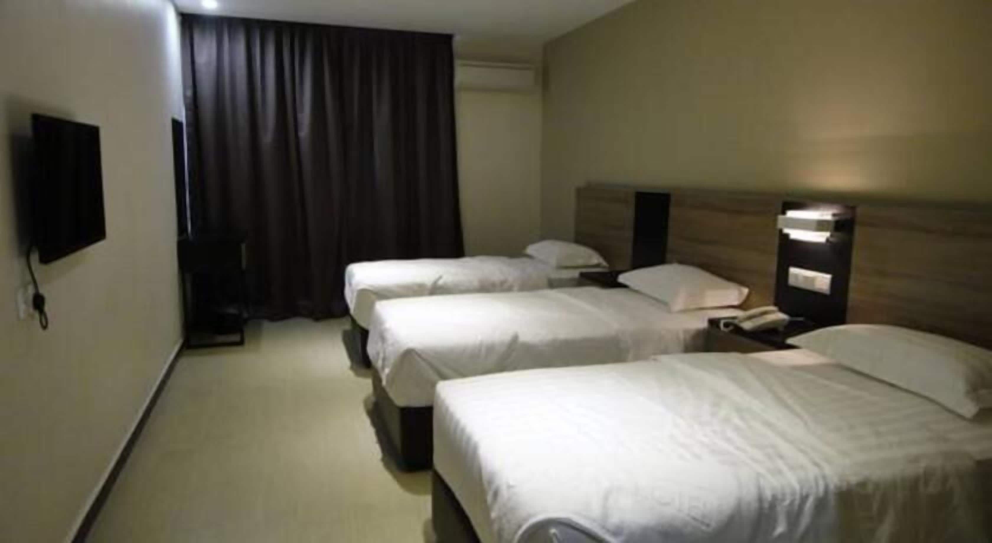 A hotel room with three beds, a flat-screen TV mounted on the wall, and a bedside table with a lamp.