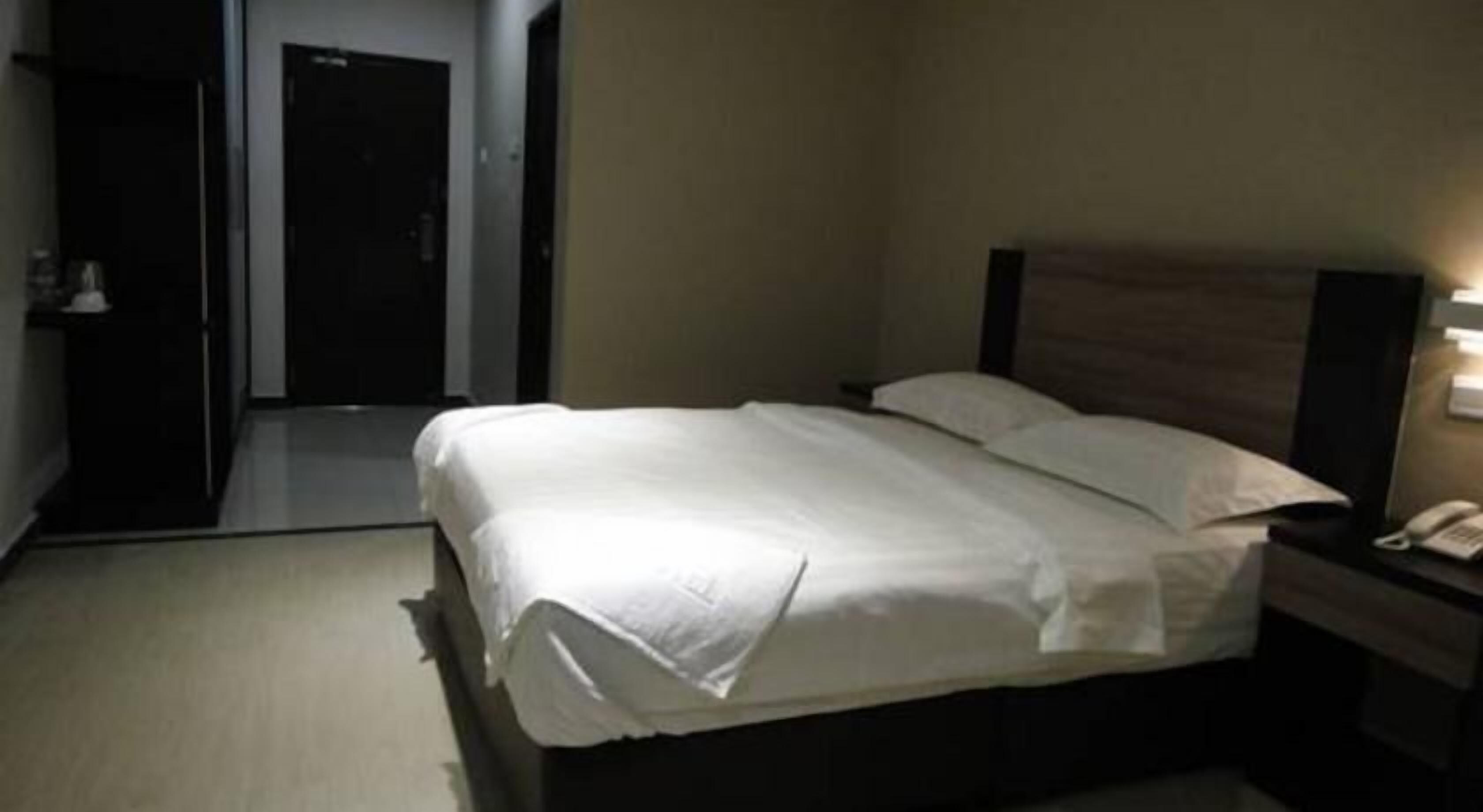 A hotel room with a bed, a nightstand with a phone, and a door leading to another room.