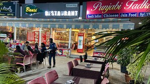 Un restaurante al aire libre con mesas y sillas, un refrigerador de Coca-Cola y un letrero que dice Punjabi Tadka.
