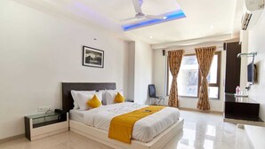 Una habitación de hotel moderna con una cama grande, una mesita de noche, un ventilador de techo y una ventana con cortinas.