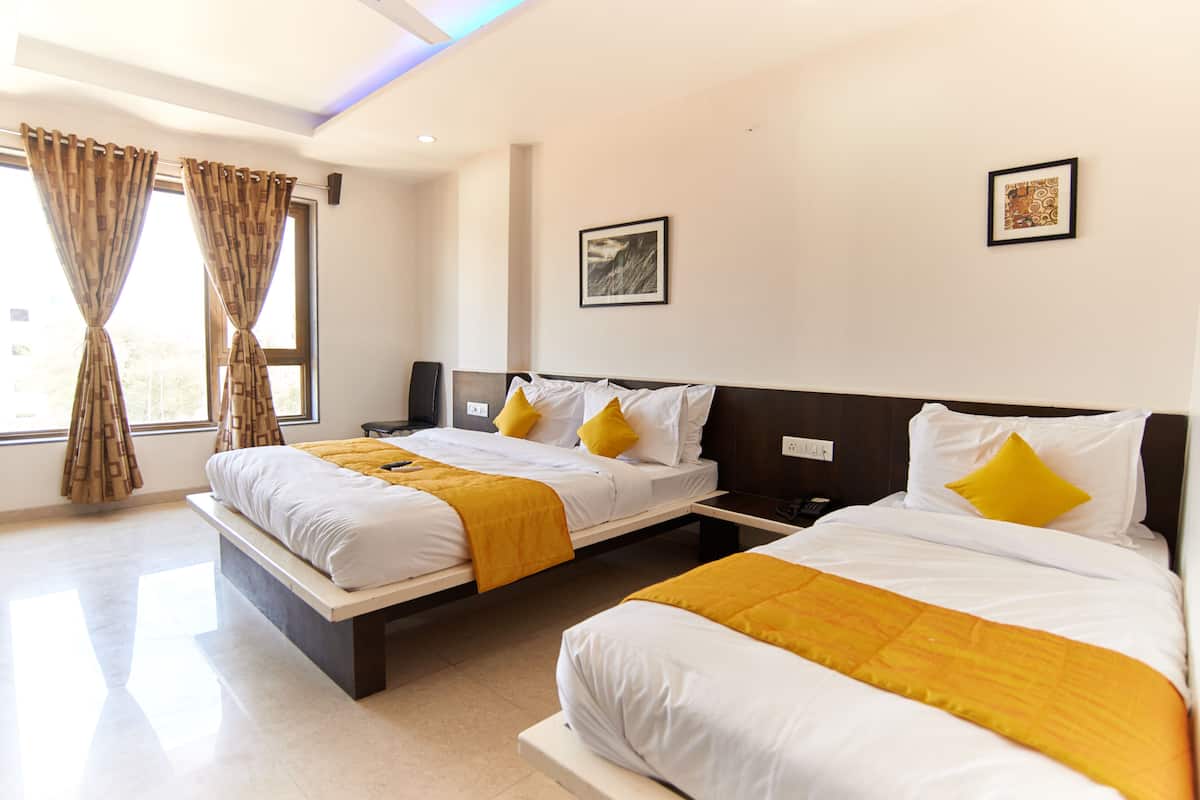 A hotel room with two beds, each with white bedding and yellow throw blankets, a nightstand, and a framed picture on the wall.