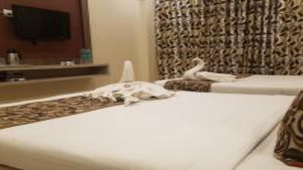 A hotel room with two beds, a television on the wall, and a patterned curtain. - Hotel Sai Chhatra (Rahata)