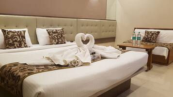 A hotel room with two beds, a bedside table with toiletries, and a heart-shaped towel on the bed.