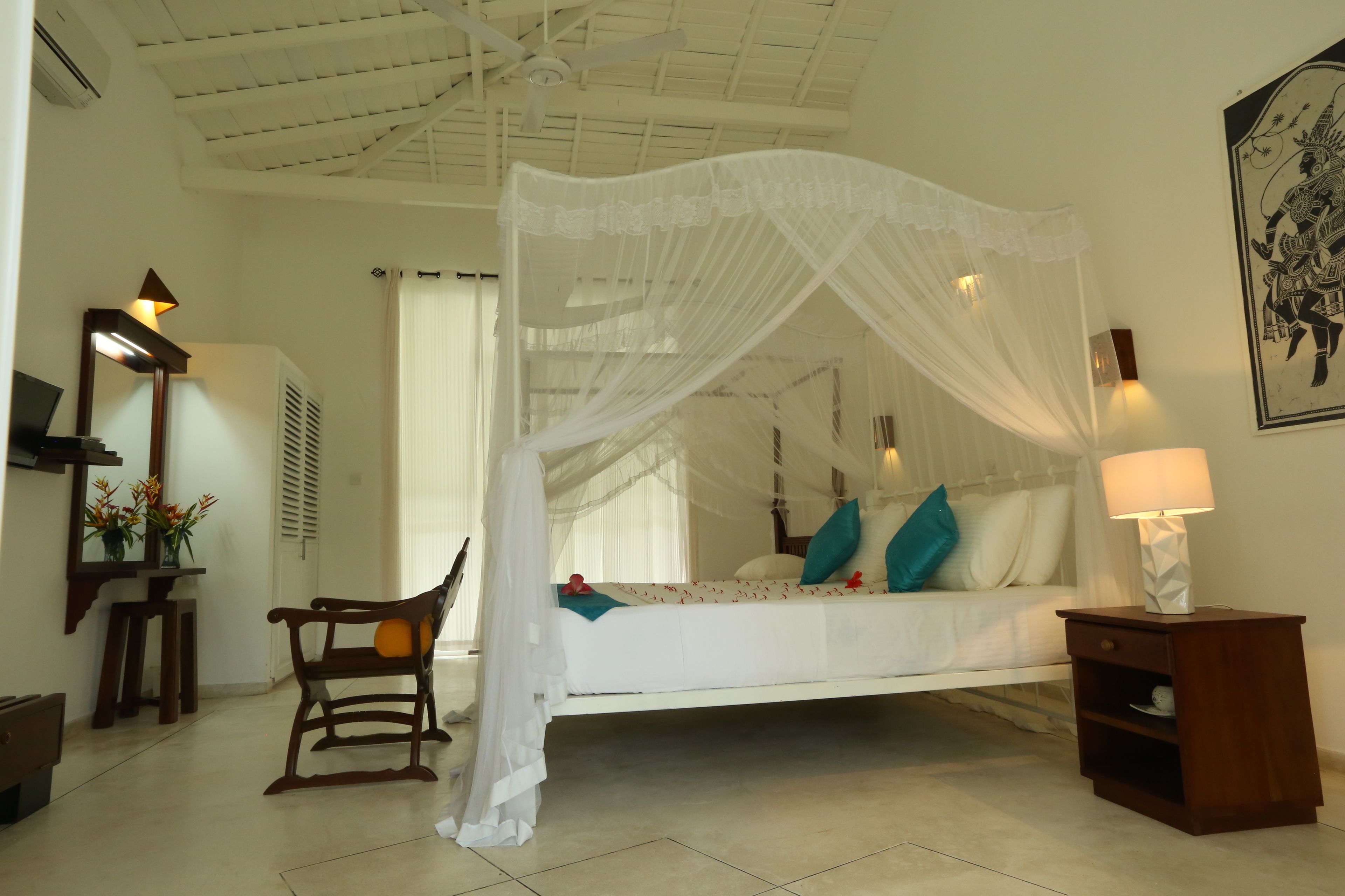A bedroom with a four-poster bed, a wooden rocking chair, a nightstand with a lamp, and a wall-mounted mirror.