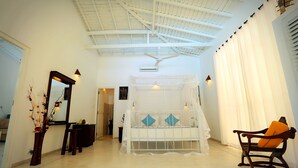 A room with a bed under a canopy, a chair with an orange cushion, a mirror, and a vase with branches. - Beach Grove Villas (Unawatuna)