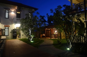 A well-lit pathway leading to a building with a balcony and a small garden area. - Hoi An Red Frangipani Villa (Da Nang)