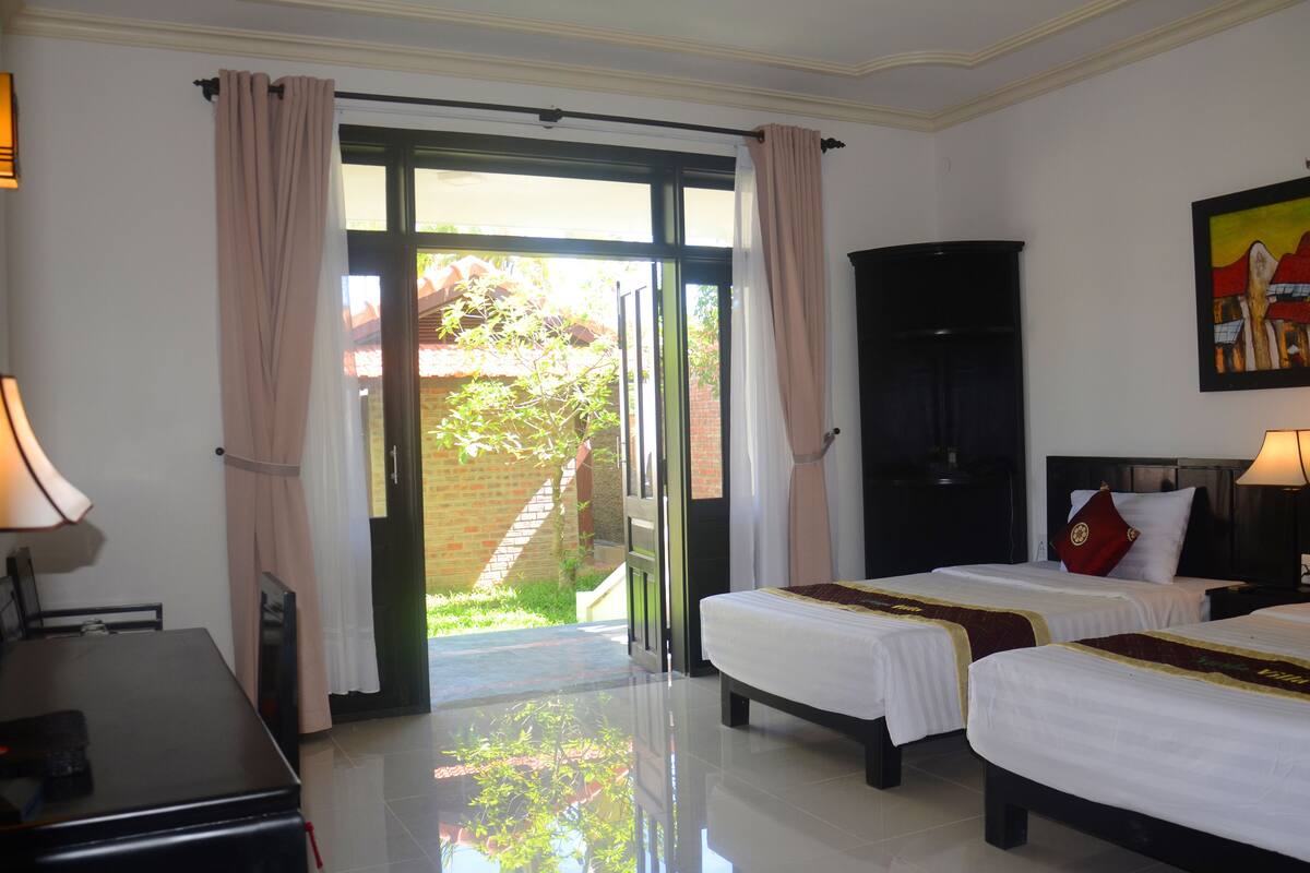 A hotel room with two beds, a desk, a chair, a black wardrobe, and a painting on the wall.