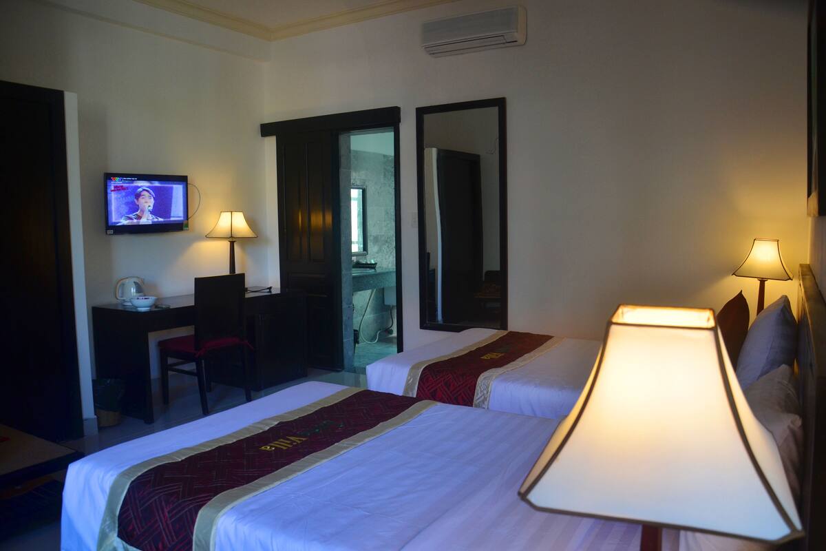 A hotel room with two beds, a desk, a chair, a television, and two lamps.