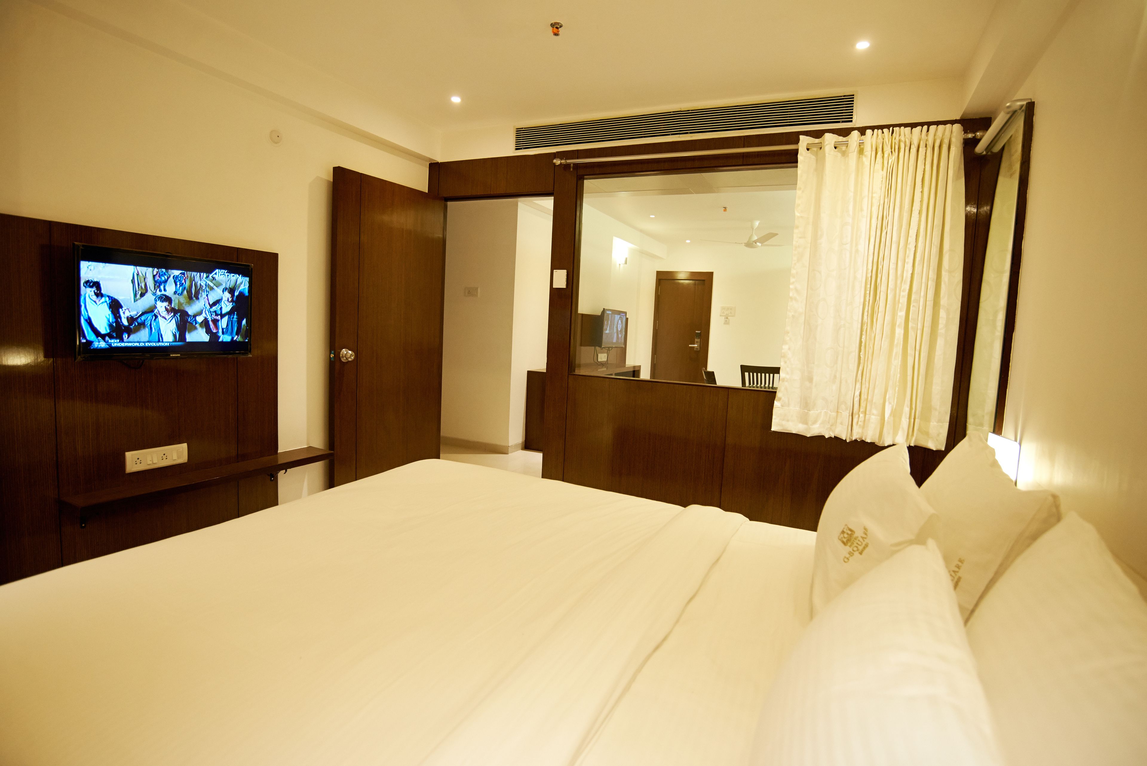 Une chambre d’hôtel avec un grand lit, un téléviseur fixé au mur et un miroir avec un rideau.