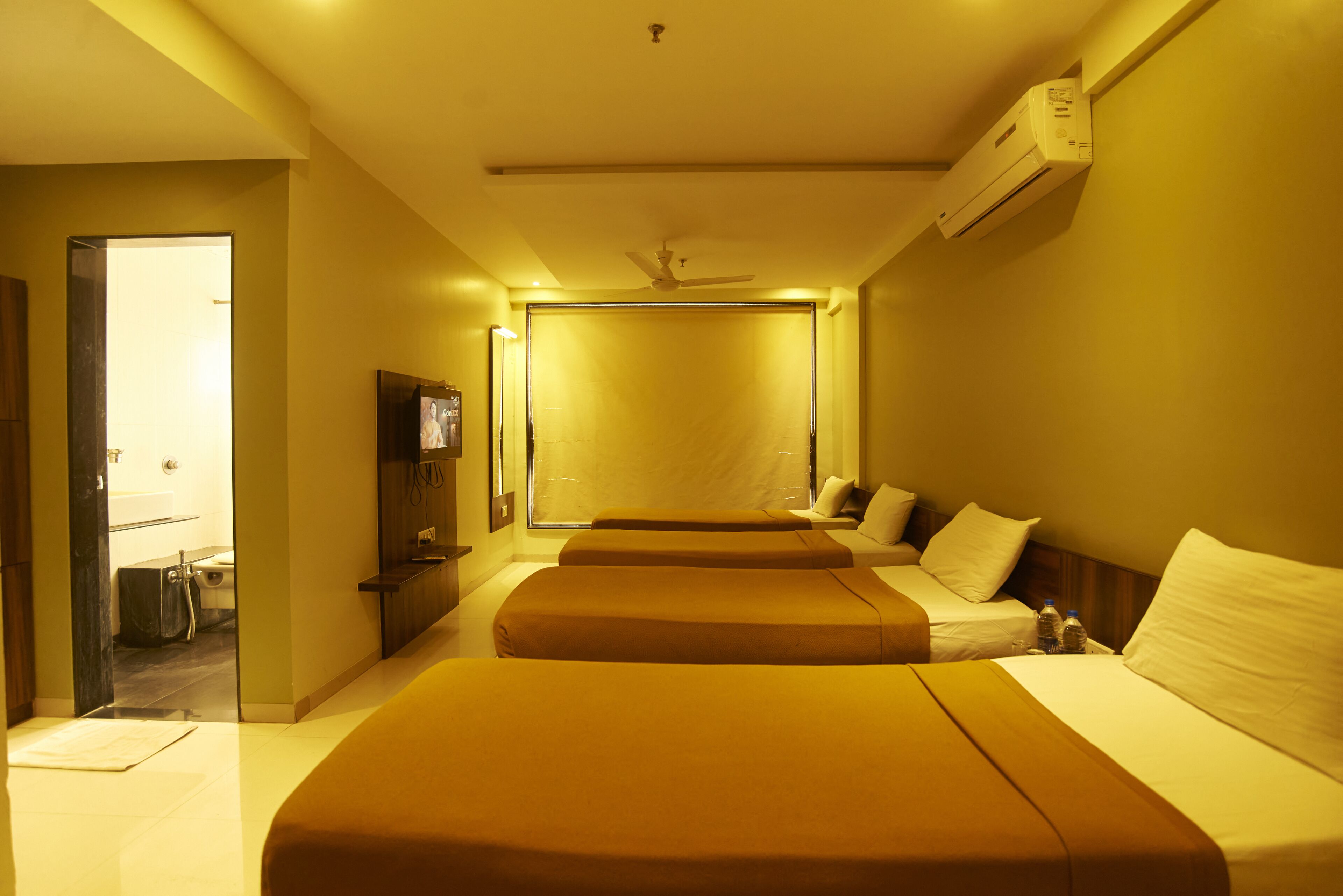 Ein Hotelzimmer mit zwei Betten, einem Deckenventilator, einer Klimaanlage und einem durch eine offene Tür einsehbaren Badezimmer.