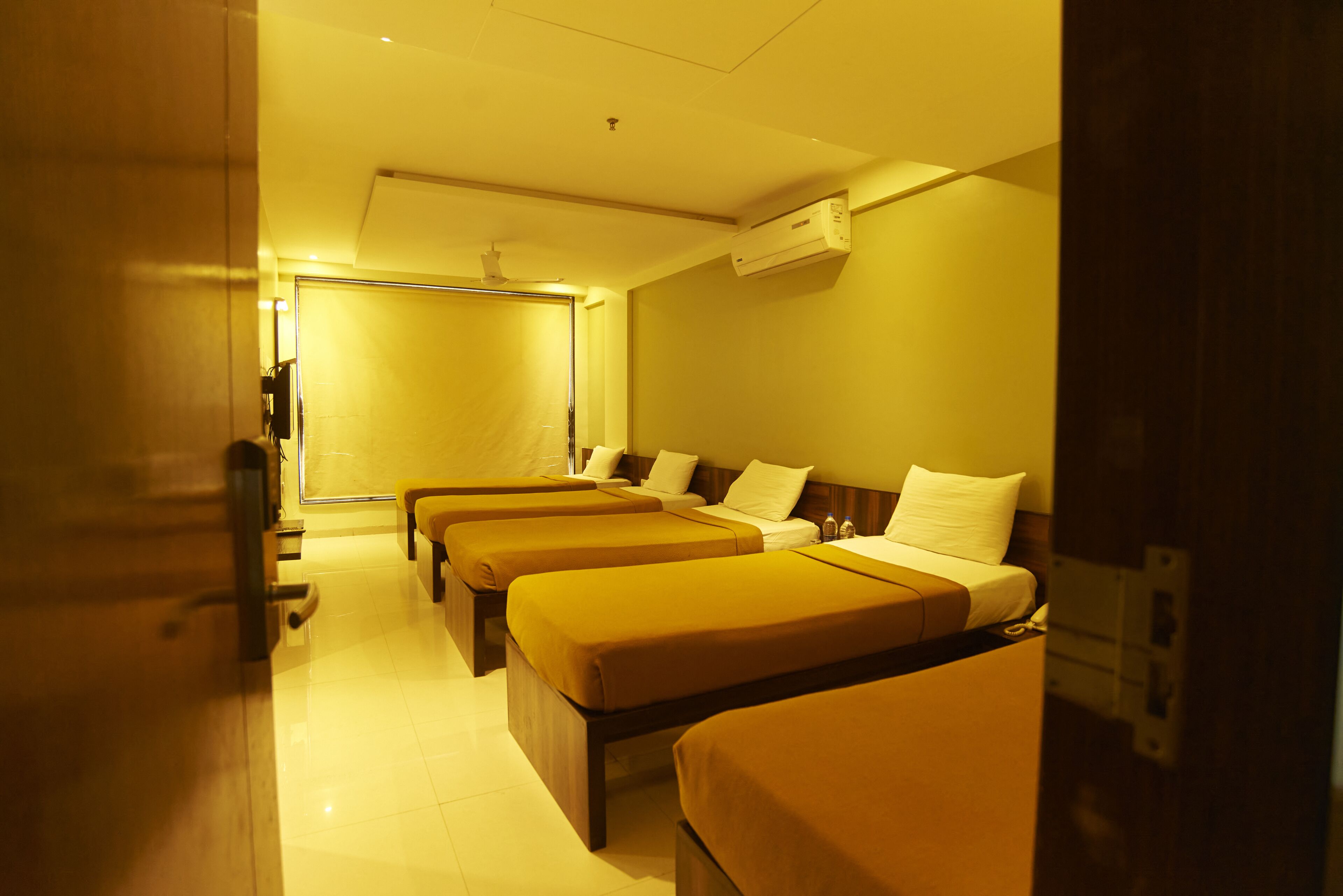 A hotel room with three single beds, a bedside table, and a large window.