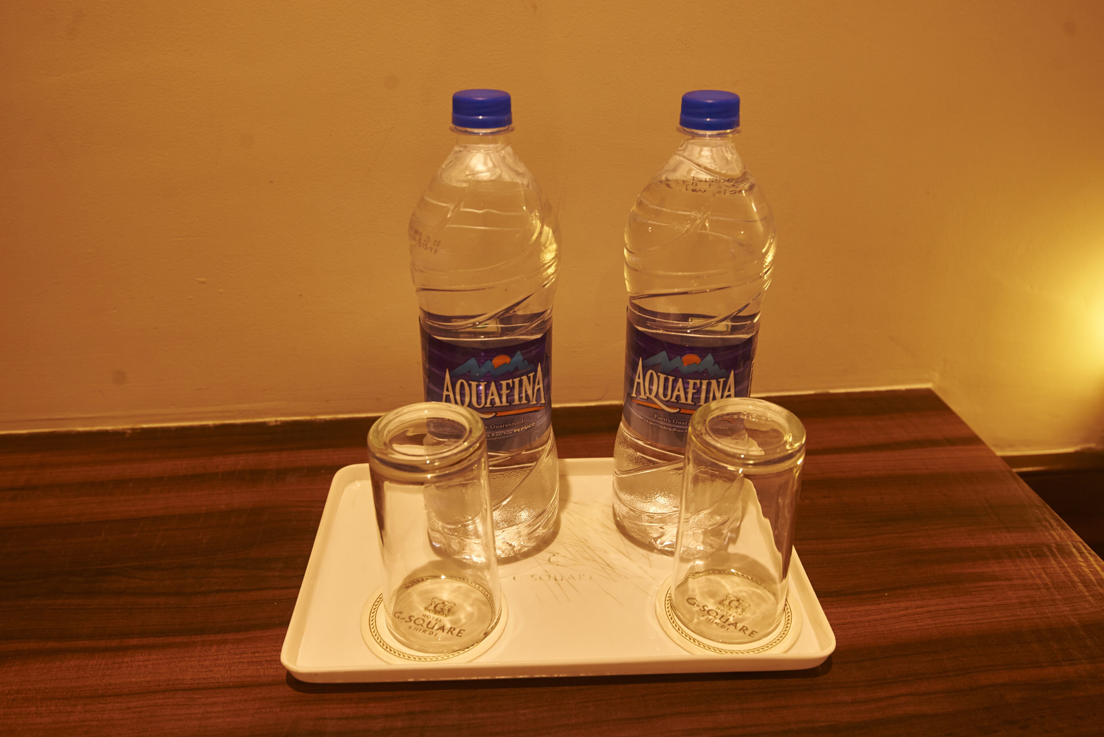 To Aquafina vandflasker og to tomme glas på et fad.