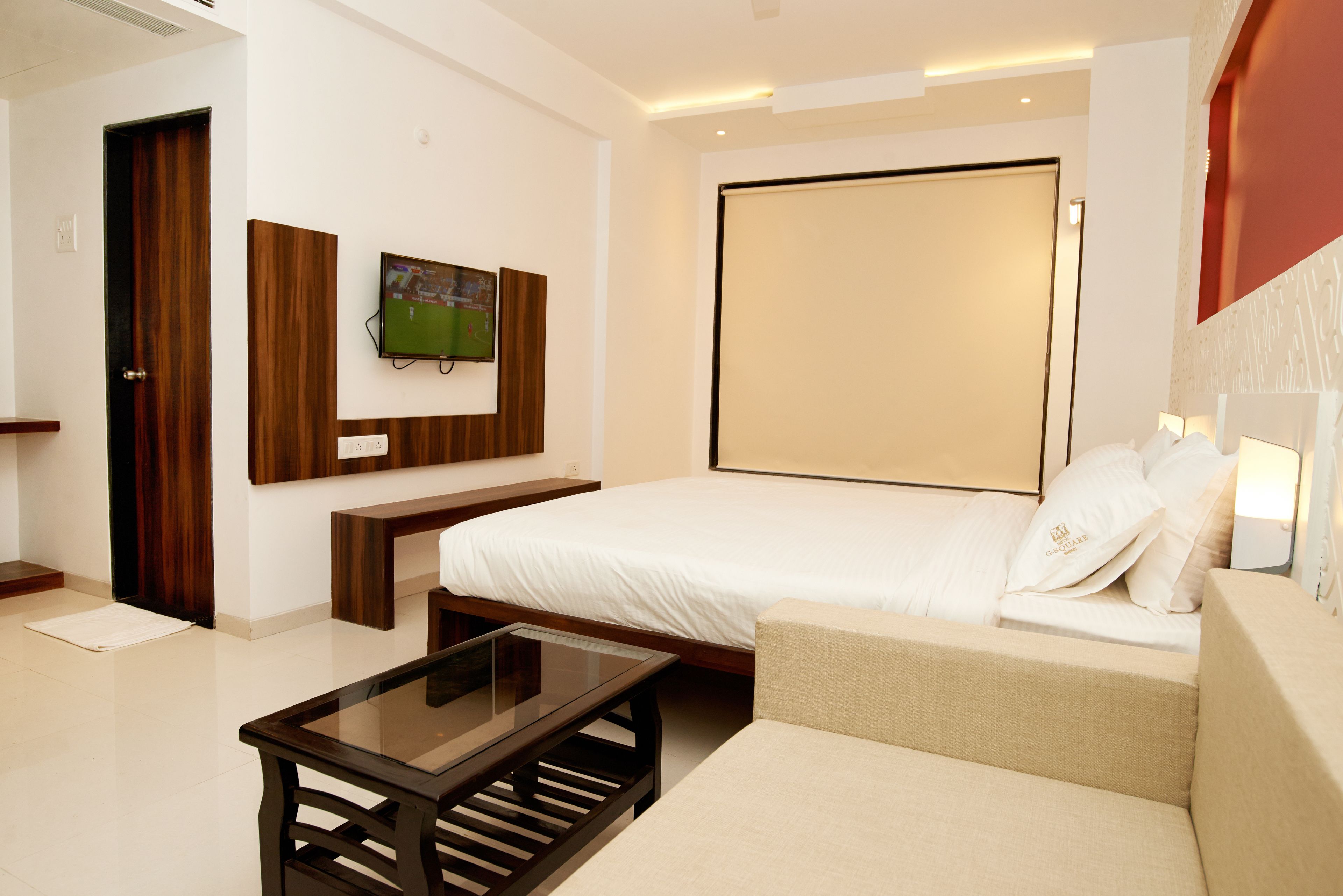Ein modernes Hotelzimmer mit einem großen Bett, einem an der Wand montierten Fernseher, einer hölzernen Bank und einem Glastisch.