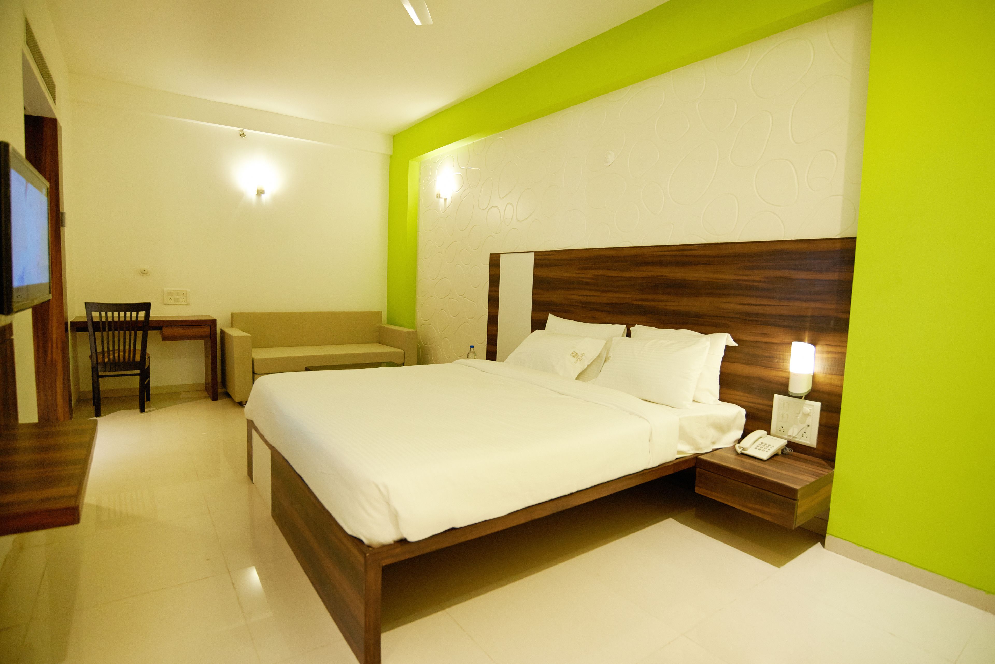 A hotel room with a large bed, bedside table with a phone, a chair, and a small desk with a chair.