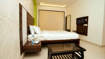 Una habitación de hotel moderna con una cama, una mesita de cristal, una mesita de noche con una botella y un televisor en la pared.