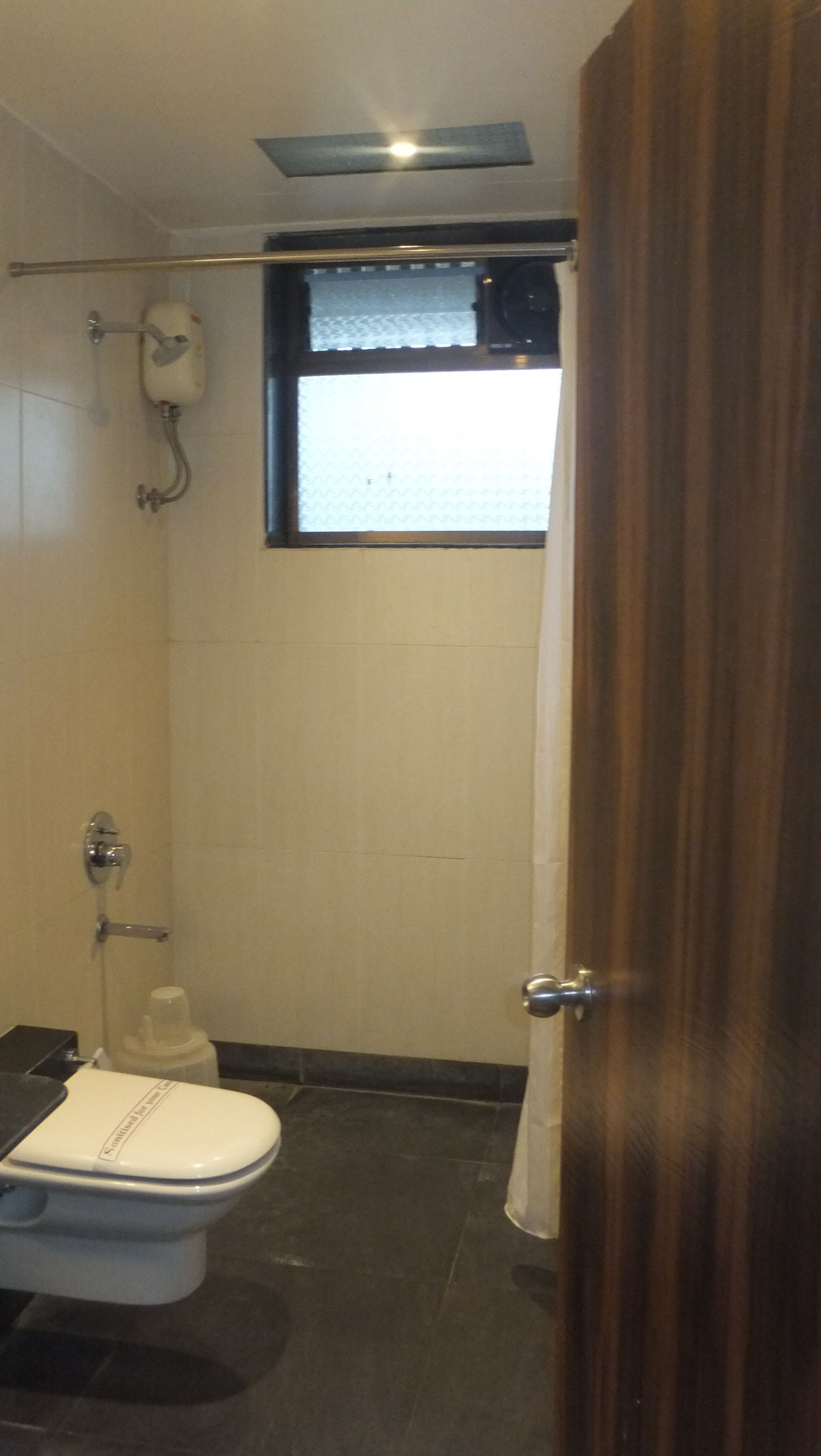 A small bathroom with a toilet, a shower, and a window.
