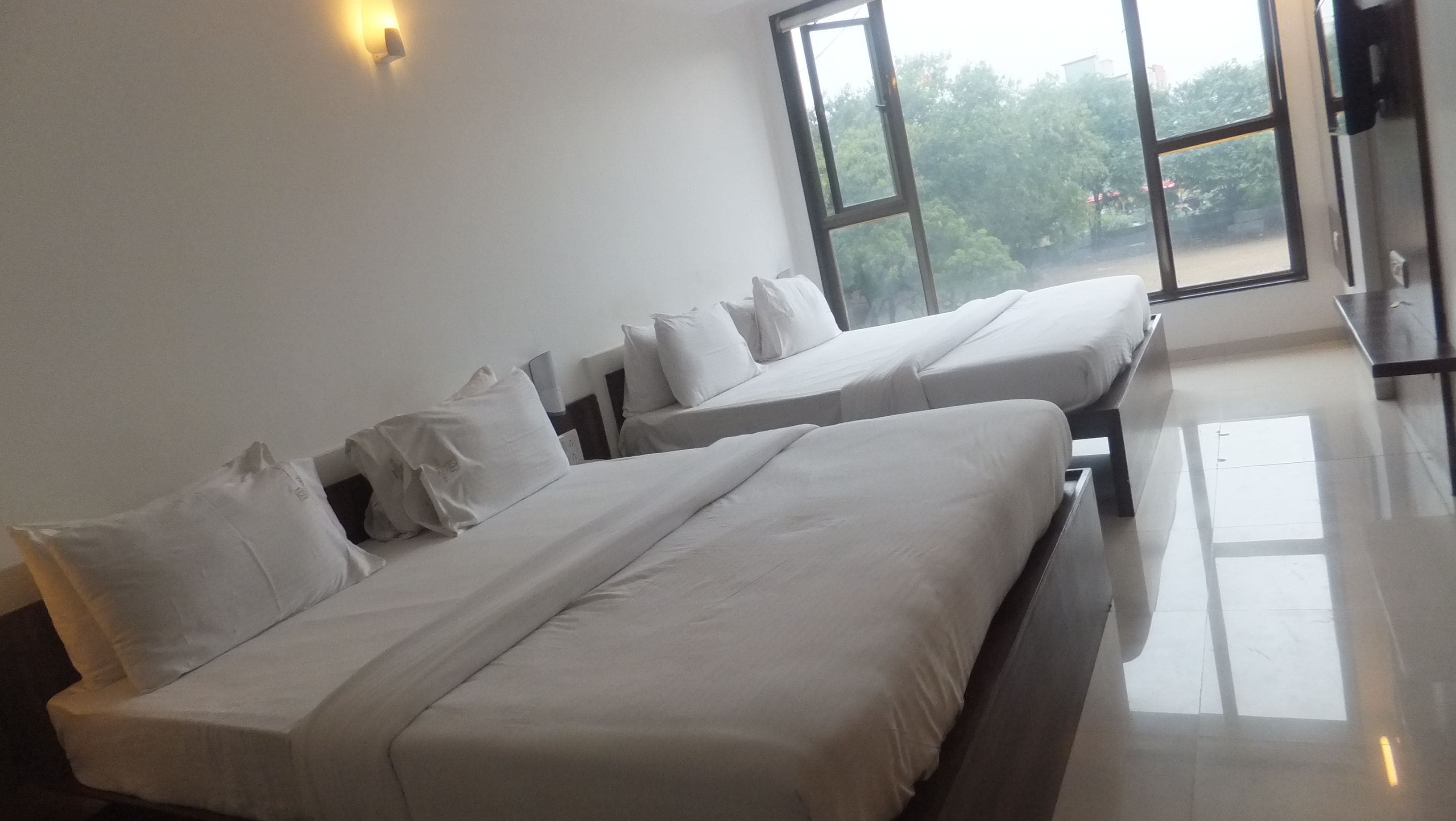 A hotel room with two beds, a large window, and a view of greenery outside.