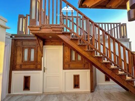 A wooden staircase leading to a door with a small window, part of a building with a white exterior and wooden accents.