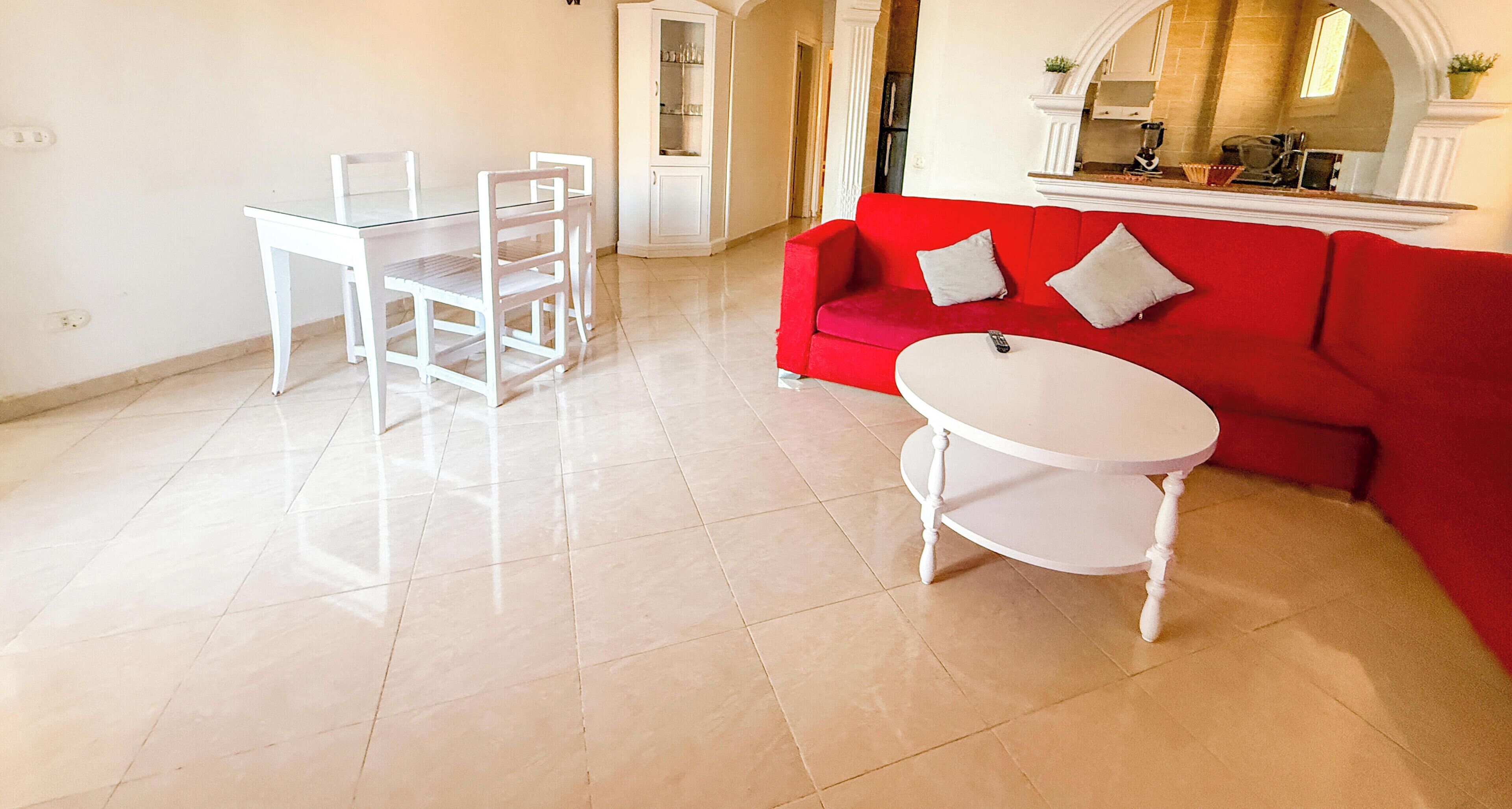A living room with a red sofa, a white coffee table, and a glass dining table with chairs.