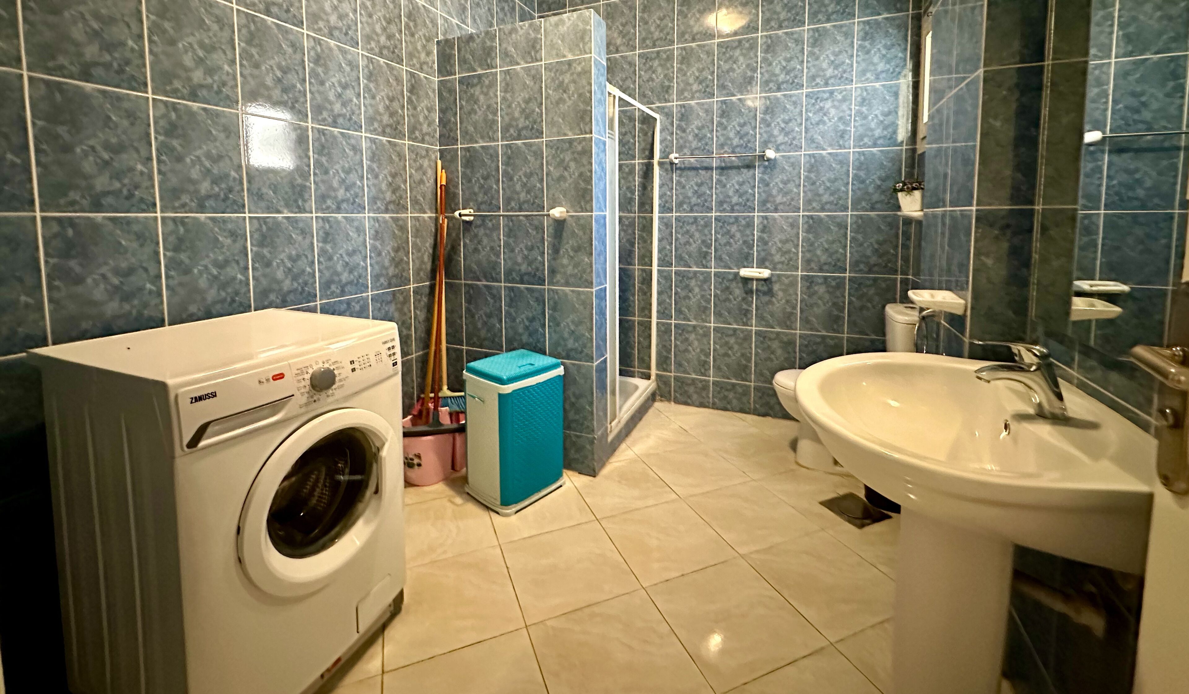 A bathroom with a washing machine, a sink, and a shower area.