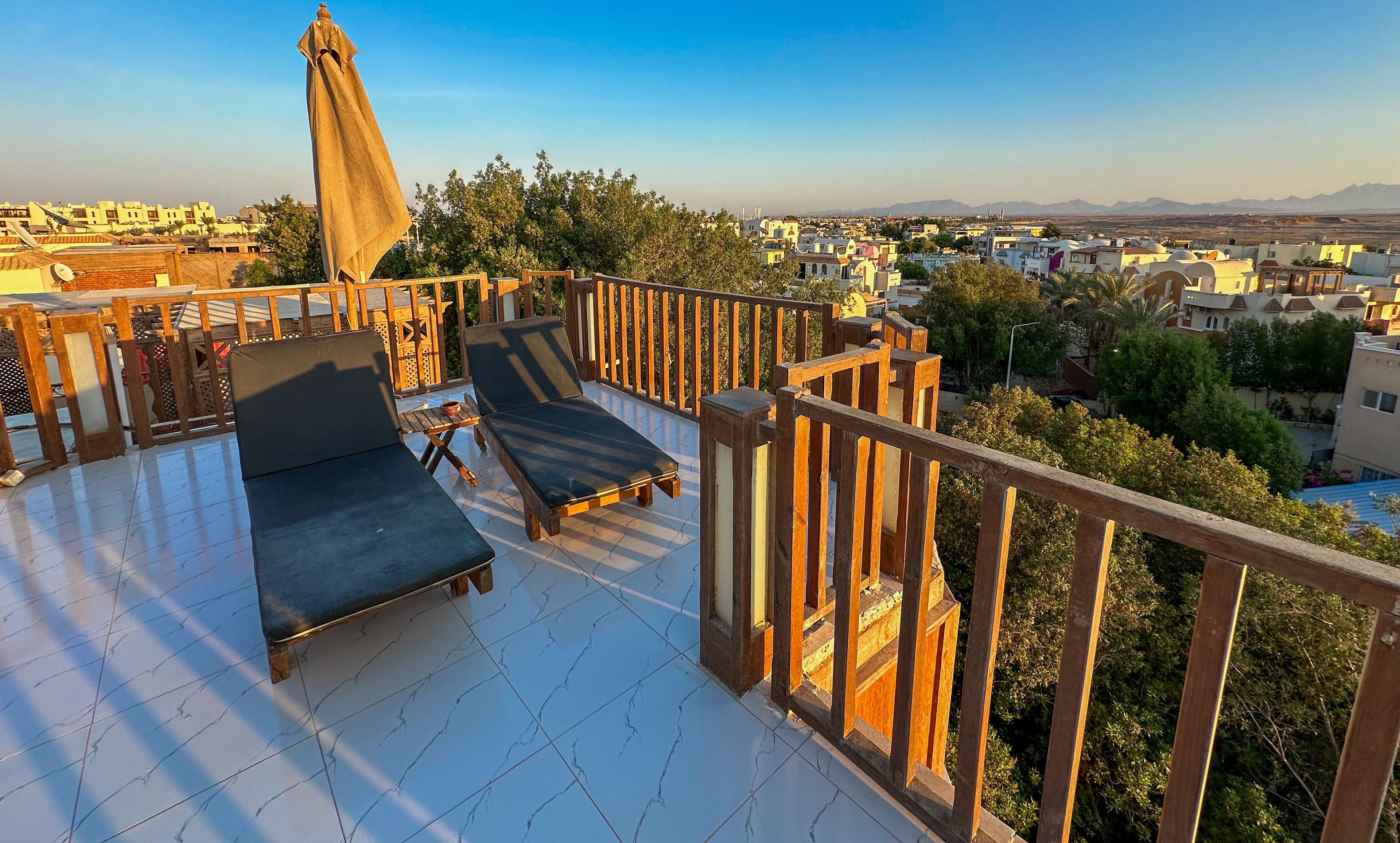 Een balkon met twee loungestoelen en een tafel, met uitzicht op een stadsgezicht van gebouwen en bergen.